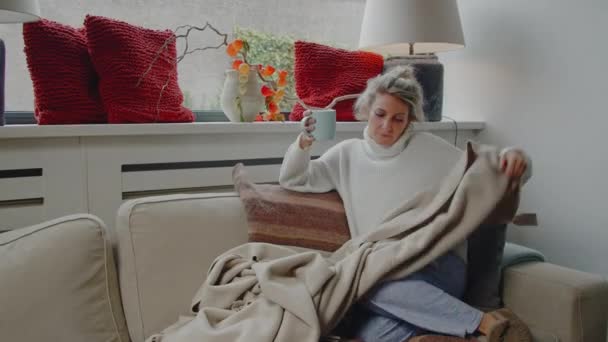 若い白人女性の快適なソファで熱いお茶やコーヒーを飲みながら 気楽で幸せな思い出について考える — ストック動画