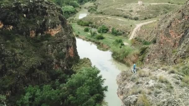 川の上の崖の端に腕を広げた男が立って景色を楽しむ — ストック動画