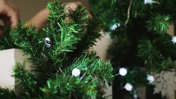 手すりに取り付けられた照明付きのガーランドのビューを閉じます ホリデーシーズンのために家を準備するときにクリスマスの装飾を掛けるために働く女性の手 白い光と松の園 — ストック動画