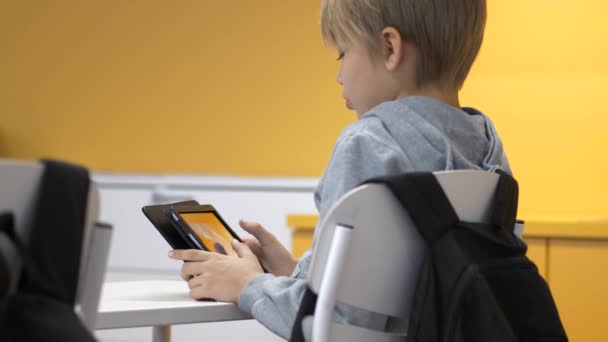 Menino Escola Jovem Olhando Para Tablet Inteligente Enquanto Sentado Uma — Vídeo de Stock