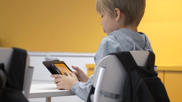 Mladý školní chlapec při pohledu na inteligentní tablet, zatímco sedí za stolem