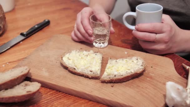 女人的手拿着一个装有伏特加的水晶杯子 一片涂了黄油和大蒜的面包躺在切碎的木板上 准备用大蒜做三明治 — 图库视频影像