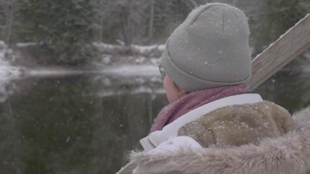 Χιόνι Πέφτει Και Κορίτσι Κάθεται Κοντά Στο Ποτάμι Απολαμβάνοντας Μοναξιά — Αρχείο Βίντεο