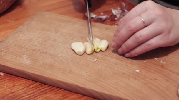 ナイフで女性の手はまな板の上にニンニクの最初のクローブを切り刻む ニンニクでサンドイッチを作る準備 閉じろ — ストック動画