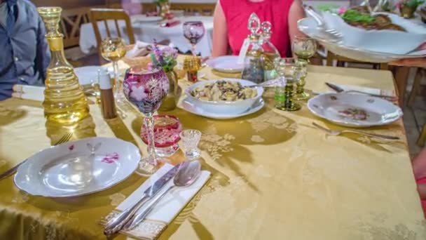 伝統的な素朴なレストランで4人のゲストとカラフルなガラスと黄金のテーブルクロスで完全にレイアウトテーブルでスロベニア料理を提供しています パンニングショット — ストック動画