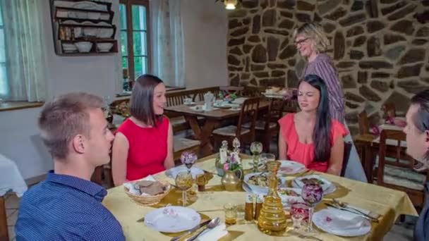 Servírka servíruje misku s jídlem u stolu se dvěma smějícími se páry, které si společně vychutnávají jídlo ve šťastné atmosféře ve staré rustikální tradiční restauraci. Snímek sledování pomalého pohybu.