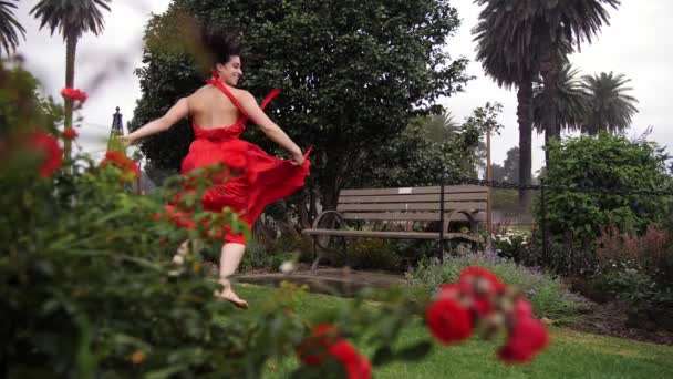 穿着红衣跳舞离开玫瑰花园的美丽女舞蹈家 — 图库视频影像