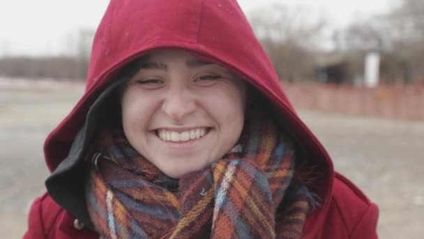 Mladá žena v červené kapuci ukazuje šťastný obličej s širokým jasným úsměvem - zavřít záběr