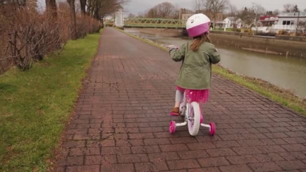 雨の後 春に運河で自転車に乗る方法を練習ピンクの愛らしい少女 スローモーション — ストック動画