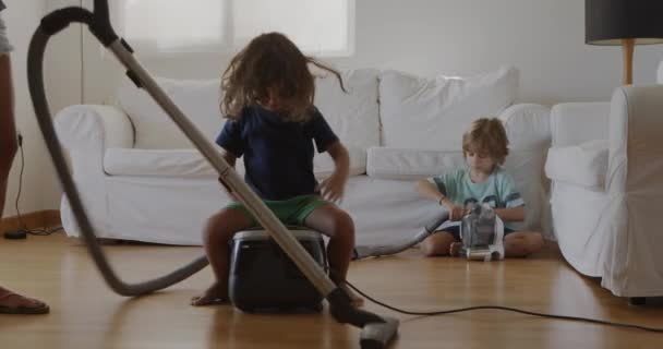 Mother cleaning the living room with a vacuum cleaner while her three year old son having fun sitting on the vacuum cleaner