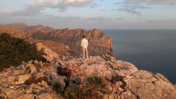 崖の上に立っている男の上を空飛ぶショットと黄金の時間で素晴らしい景色を明らかに — ストック動画