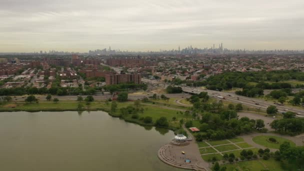 在灰蒙蒙的天气里 俯瞰公园池塘的空中景观 无人驾驶相机卡车沿着池塘慢慢地离开了 无人机的高度足以看到地平线上的曼哈顿天际线 — 图库视频影像