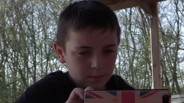Милий Молодий Хлопчик Сидить Надворі Граючи Своєму Смартфоні — стокове відео