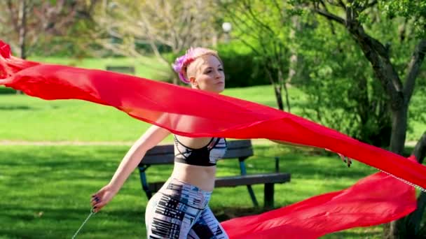 An attractive woman twirls red voi poi veils performing in the park - in slow motion.