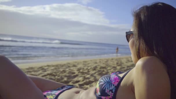 Gyönyörű fiatal nő bikiniben fekszik a tengerparton, és néz a víz felett