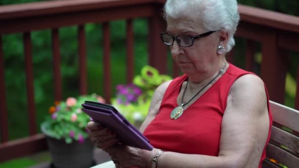 電子書籍を読む森の中のデッキの外に座っている高齢者の女性の前の銃撃からの閉鎖 — ストック動画