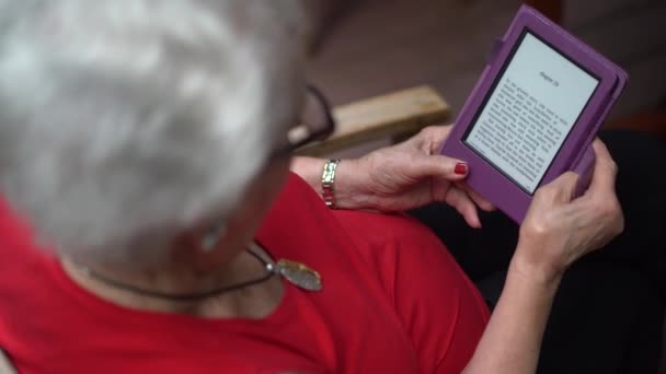 Extrém közelkép egy idős nő vállán, aki kint ül az erdőben, és e-bookot olvas..