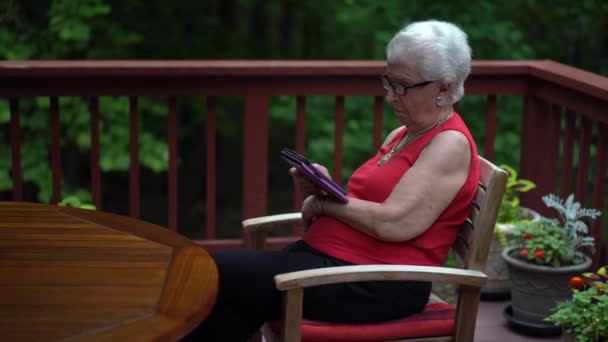 森の中のデッキに座って電子書籍を読んでいる高齢女性 — ストック動画