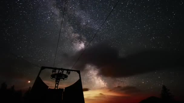 4k time lapse video of the milky way with clouds in the Austrian Alps. In the front is an old ski lift.