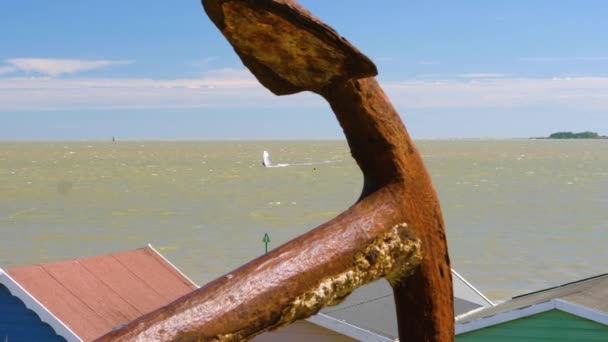 梅尔西岛上的风冲浪者 前方有一个生锈的锚 可以看到海滩上的茅屋 — 图库视频影像