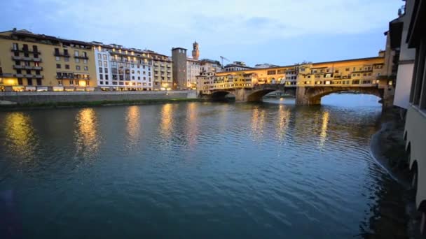 Wide shot of the famous Ponte Vecchio in Florence, Tuscany, Italy at dusk and its reflection on the windows of a building on the Arno river embankment.