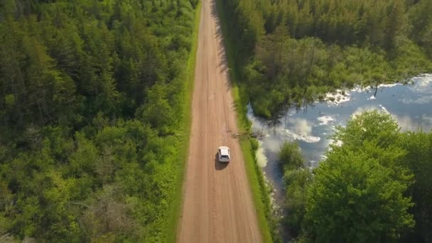 Aerial of white car driving down dirt road towards beautiful farmland