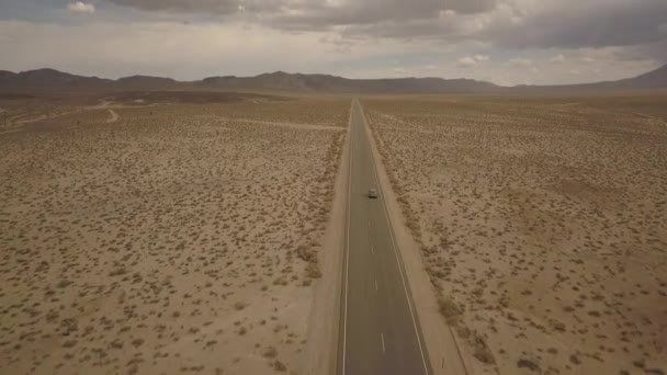 Aerial overview of car driving thru road in California desert - dynamic tilt up to cloudy sky