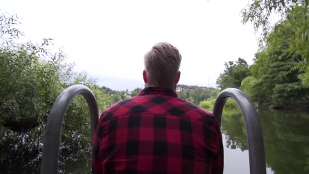 スウェーデンの静かな湖で景色を楽しんで座っている男 安定したグライドカムスローモーション映像 カメラはモデルから遠ざかります 美しい自然景観 — ストック動画