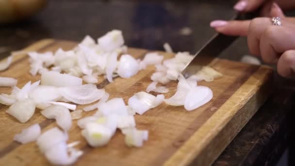 A females hands finishing up dicing an onion on a wooden cutting board using a sharp knife.