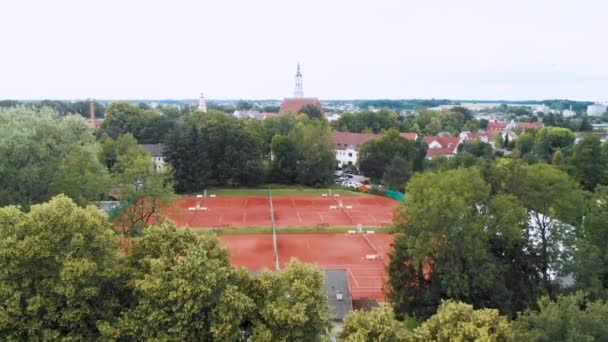 Vzdušný bezpilotní letoun stoupající záběr hliněných tenisových kurtů a německého města v pozadí.