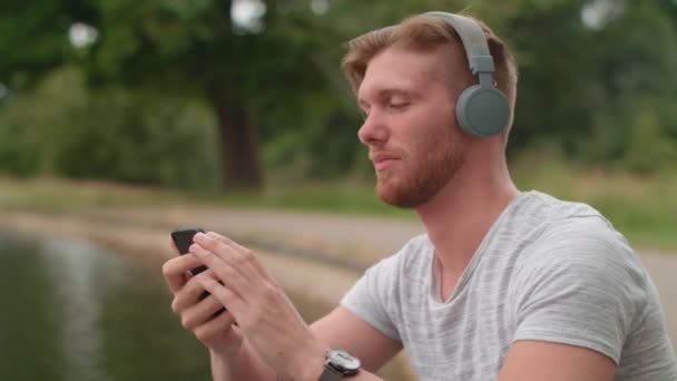 男は池で音楽を聞いて頭をうなずいて土 — ストック動画