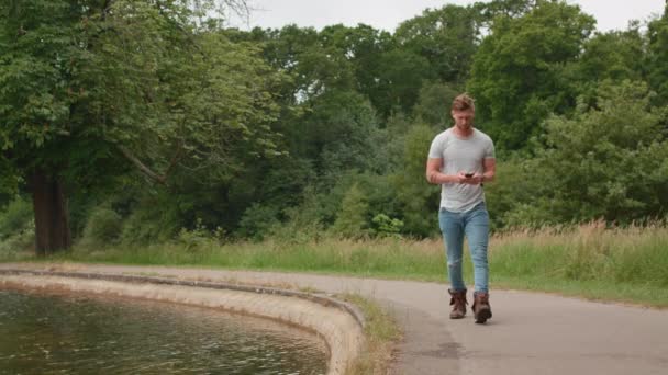 男は池のそばを歩いてリラックスするのに時間がかかる — ストック動画