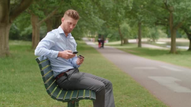 Park Bench Üzerine Oturan Adam Akıllı Telefonunu Kullanarak Çevrimiçi Ürün — Stok video