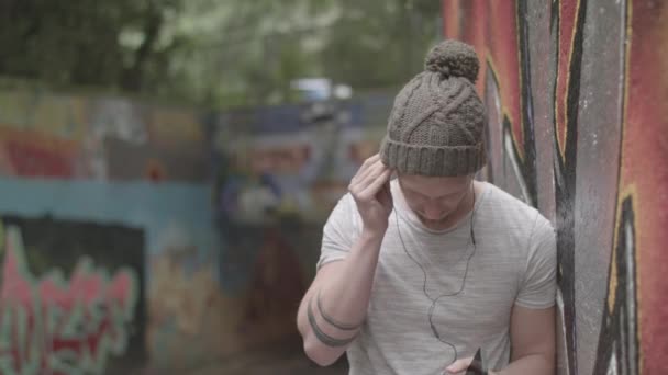 Man Die Naar Muziek Luistert Oortelefoons Terwijl Hij Tegen Graffiti — Stockvideo