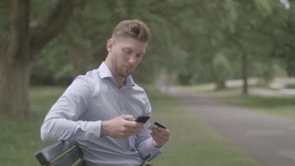 Человек Сидит Скамейке Парке Делает Покупку Помощью Своего Телефона Ungraded — стоковое видео