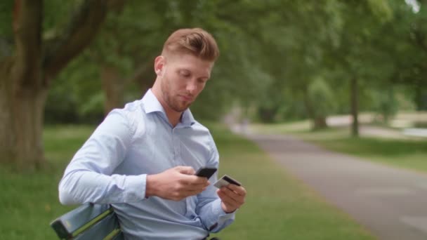 Человек Сидит Скамейке Парке Делает Покупки Помощью Своего Телефона — стоковое видео
