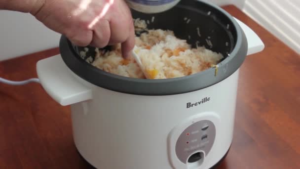 Scooping cooked rice and tomato from rice cooker into a blue bowl