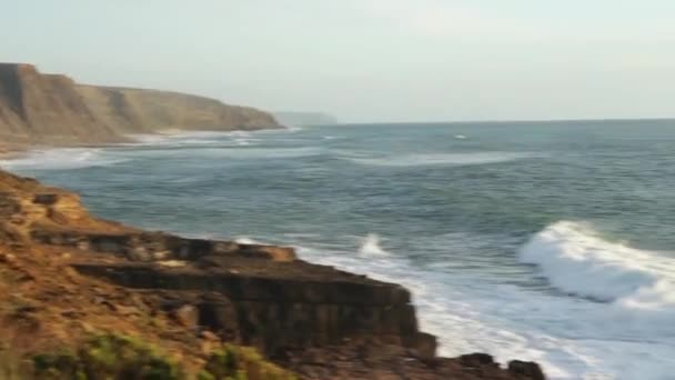 崖や霧が立ち並ぶ海岸沿いのビーチで波が打ち寄せる風景 カメラの動きを傾ける — ストック動画