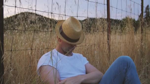 Férfi szalmakalap alatt alszik a kerítésnek hosszú fűben kék farmert és fehér inget visel