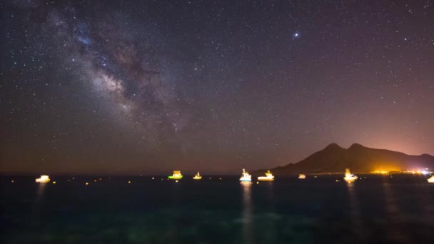 Milky way night sky in a seascape with boats and a mountain