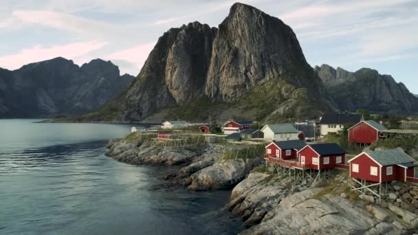 ノルウェー北部ロフトテン諸島の小さな島Hamnoy Reine から海にぶら下がっている赤い家の空中映像 背景に劇的な山々 — ストック動画