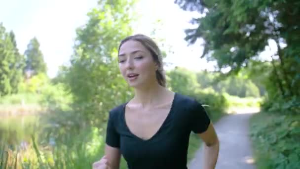 完璧な夏の日に公園で池の周りをジョギングする女性 笑顔で幸せな女の子が屋外で運動 — ストック動画