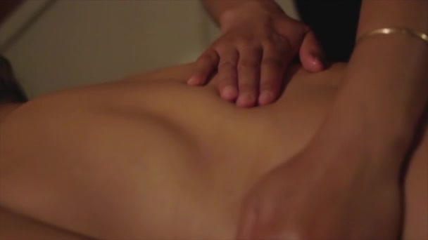 Detailní záběr rukou během masáže na zádech mladé ženy.