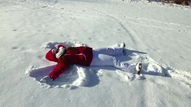 Lassított felvétel egy lányról, aki hóangyalt csinál a hóban egy fényes és napos téli délután a szabadban..