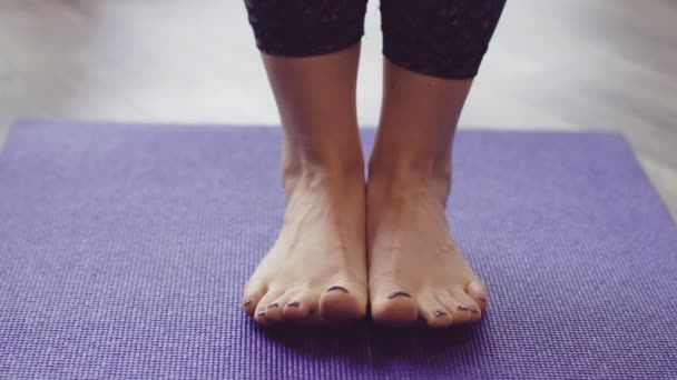 Žena s fialovým lakem na nehty vrtí prsty na fialové podložce na jógu
