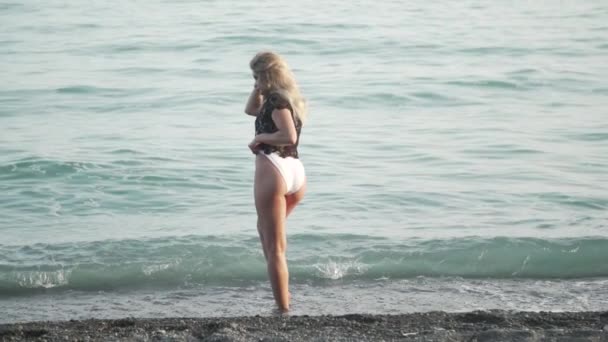 Uma Menina Jovem Loira Branca Posa Uma Praia Enquanto Ondas — Vídeo de Stock