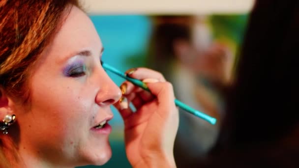 Make-up umělec dělá sexy make-up oči atraktivní ženě. Close up visagiste podání make-up pro filmovou herečku. Profesionální vzhled v kosmetickém studiu.