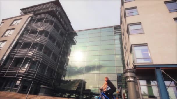 Egy narancssárga inges diák háton lovagol egy modern szürke európai egyetem épülete előtt, sok ablakkal..
