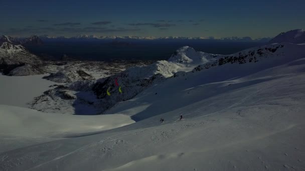 雪の山の幻想的な背景ドローンショット 灰色の雲と青い空 遠くから青い海 氷の斜面に3人のスノーキットが凧を完全に制御しています ノルウェー4K 30Fps — ストック動画