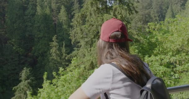 一位美丽的年轻女子站在一座桥上欣赏森林的美景 她转过身来 对着摄像机笑 — 图库视频影像